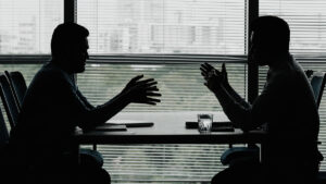 Silhueta de dois executivos frente a frente em uma mesa de negociação corporativa B2B.