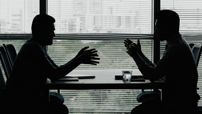 Silhueta de dois executivos frente a frente em uma mesa de negociação corporativa B2B.