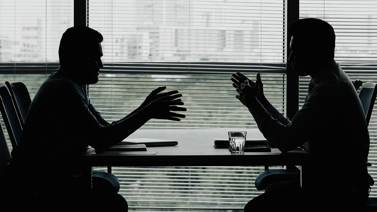 Silhueta de dois executivos frente a frente em uma mesa de negociação corporativa B2B.